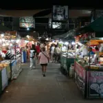 Shoppers walking between food stalls at a night market in Rayong, Thailand