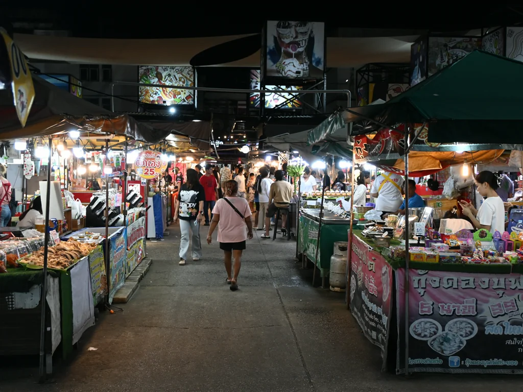 Shoppers walking between food stalls at a night market in Rayong, Thailand